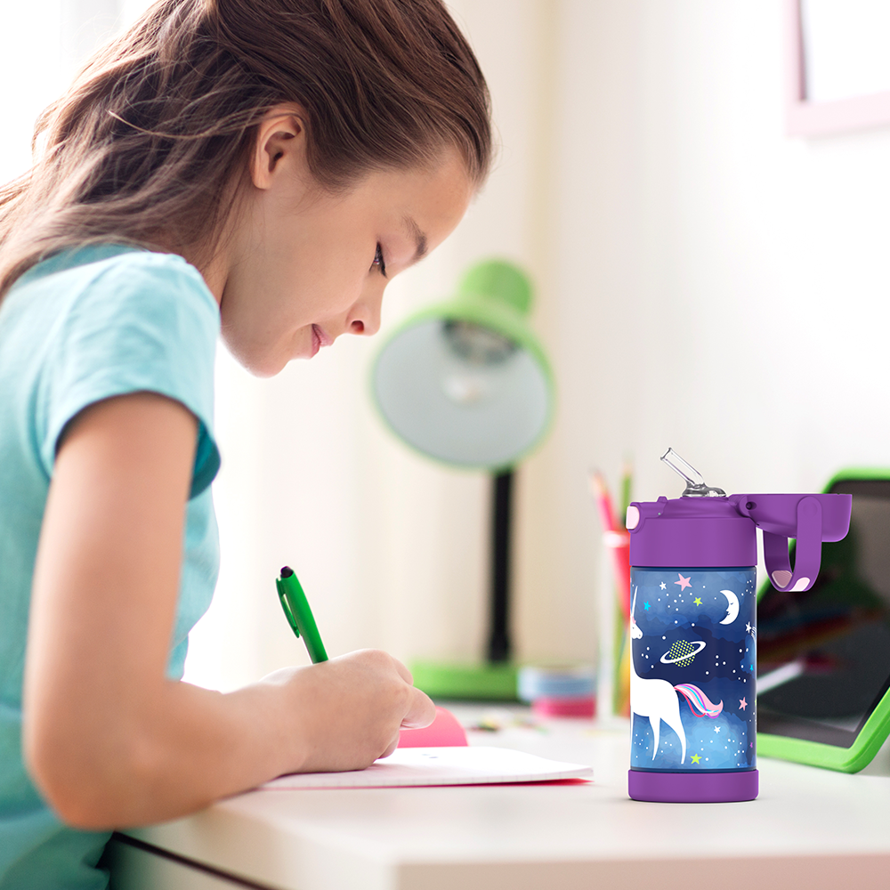 Girl sitting at a table doing homework, with a 12 ounce Space Unicorn Pattern Funtainer water bottle opened next to her.