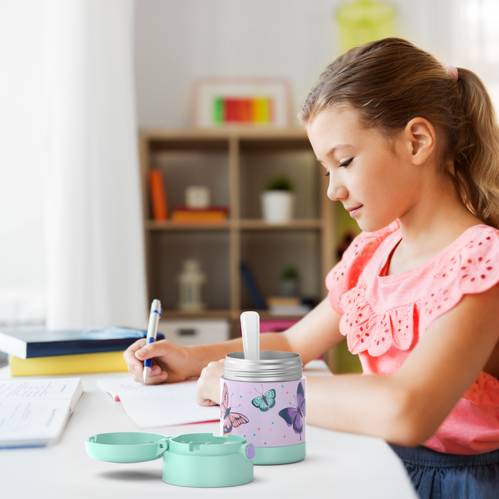 Girl sitting at table doing homework with an open 10 ounce Funtainer pastel butterflies pattern food jar open next to her.