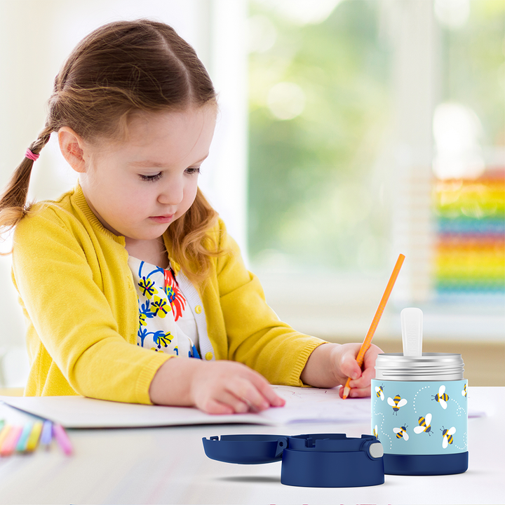 Girl sitting at table coloring with an open 10 ounce Funtainer honey bee pattern food jar open in front of her. 