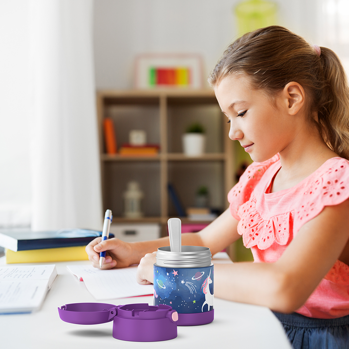 Girl sitting at table doing homework with an open 10 ounce Funtainer unicorn in space pattern food jar open next to her.