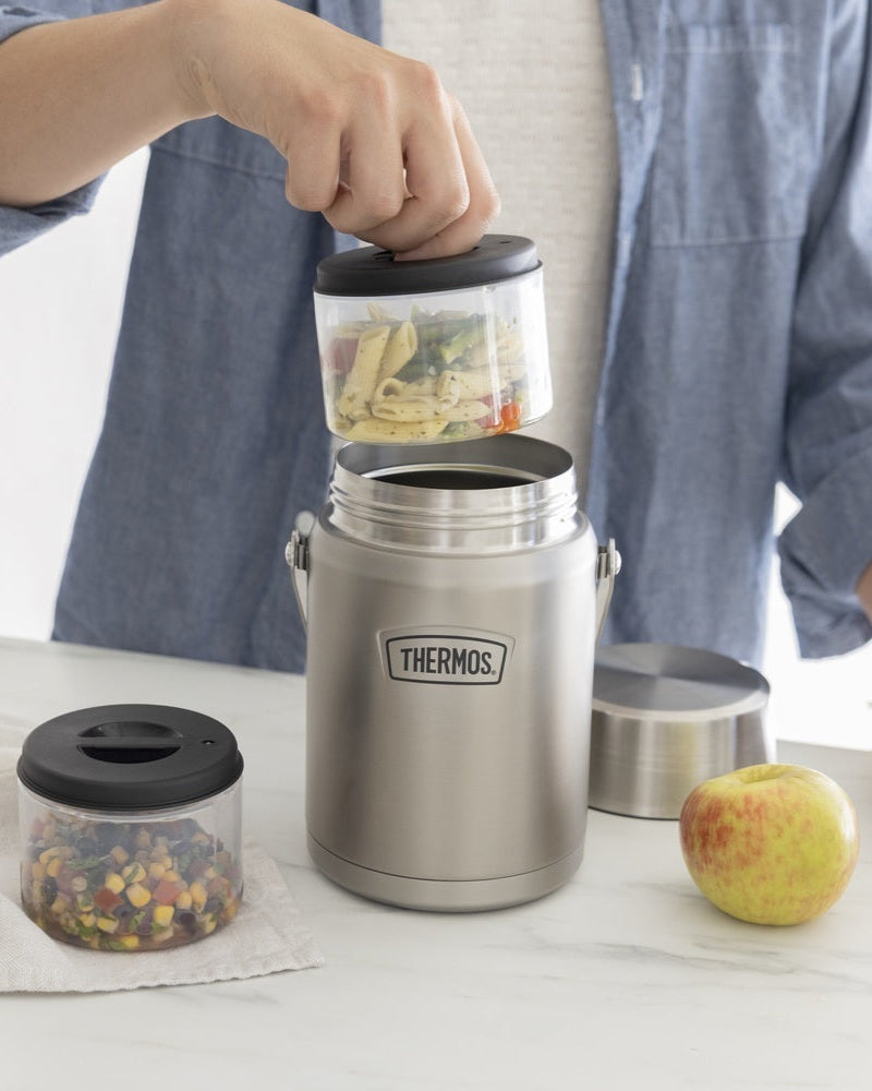 Person using a Thermos Icon 47oz Food Jar pulling out the included containers filled with food on a table with an apple and other containers.