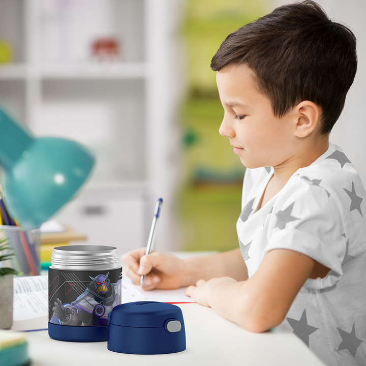 Boy sitting at table doing homework with an open 10 ounce Funtainer food jar open next to him.
